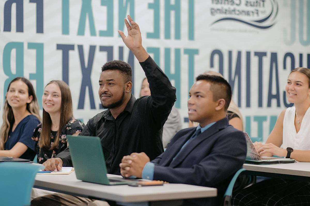 Student raises his hand in classroom lecture.